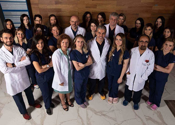 Eine Gruppe von Ärzten und medizinischem Personal in weißen Kitteln und blauen Uniformen posiert für ein Gruppenfoto in einem modernen Klinikgebäude.